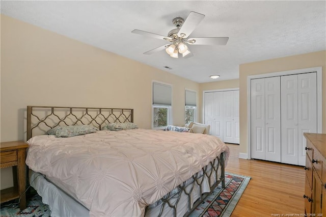 bedroom featuring light wood-style floors, ceiling fan, visible vents, and two closets