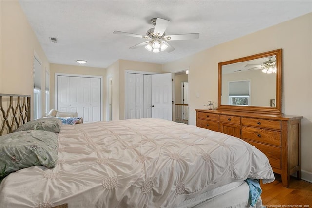 bedroom with ceiling fan, wood finished floors, visible vents, and multiple closets