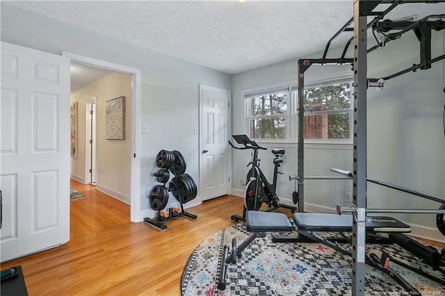 exercise area featuring a textured ceiling, baseboards, and wood finished floors