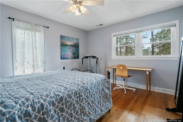 bedroom with baseboards, multiple windows, visible vents, and wood finished floors