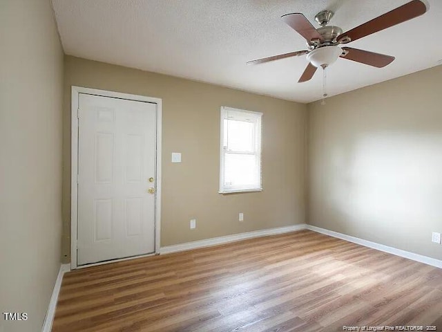 spare room with a textured ceiling, light wood finished floors, a ceiling fan, and baseboards