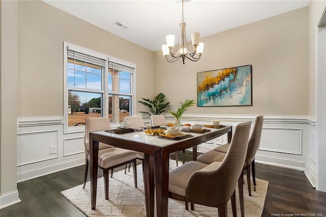 dining area with dark wood-style floors, visible vents, a decorative wall, an inviting chandelier, and wainscoting