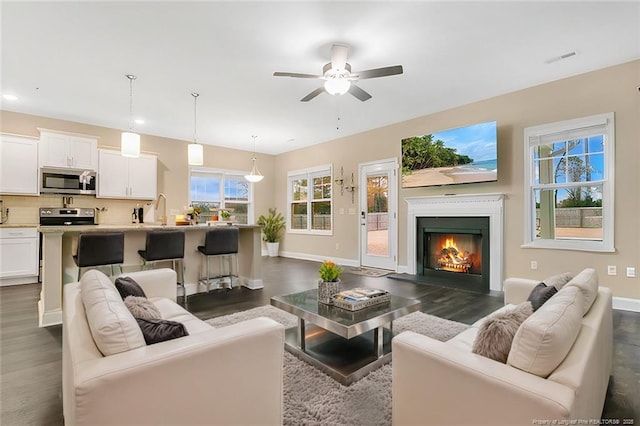 living room with a lit fireplace, dark wood finished floors, visible vents, and baseboards