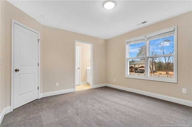 unfurnished bedroom featuring carpet, ensuite bath, visible vents, and baseboards