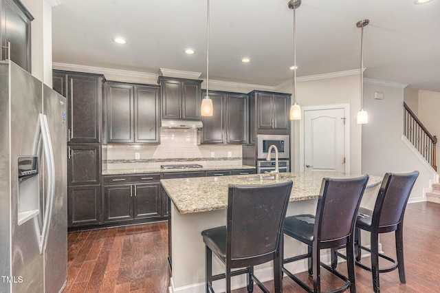 kitchen with light stone counters, under cabinet range hood, appliances with stainless steel finishes, dark wood-style floors, and tasteful backsplash