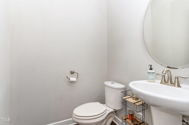 half bathroom featuring toilet, baseboards, and a sink