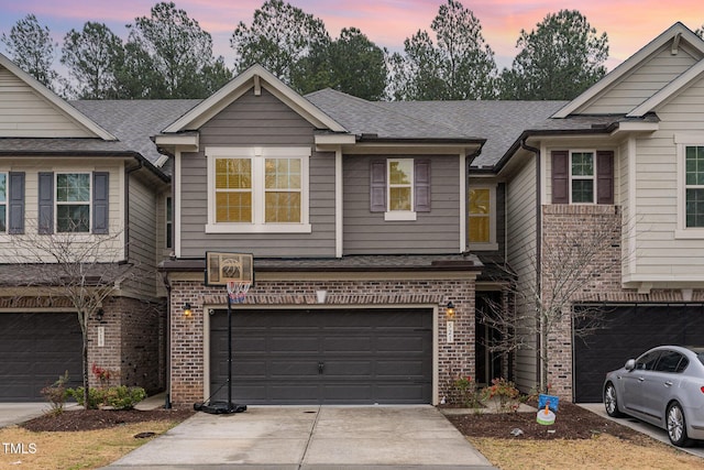 multi unit property featuring brick siding, driveway, an attached garage, and roof with shingles