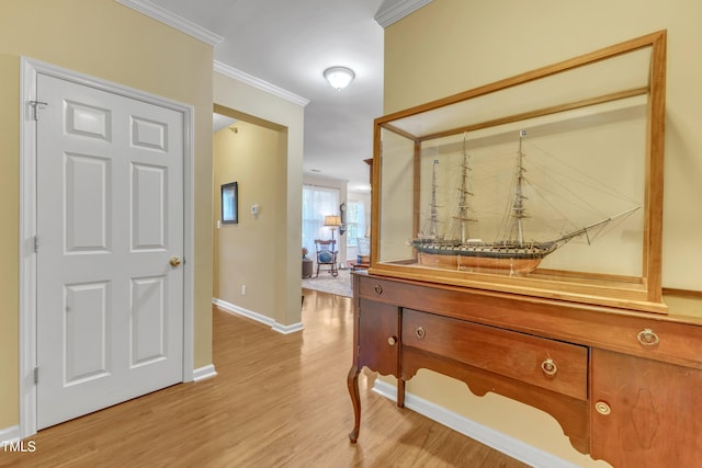 hallway with ornamental molding, light wood-style flooring, and baseboards