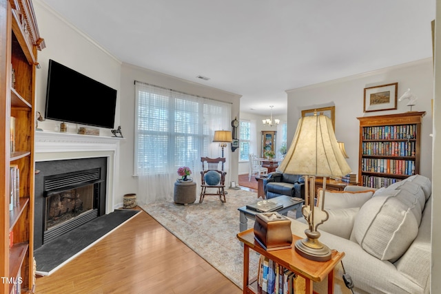 living area with a fireplace with raised hearth, crown molding, an inviting chandelier, and wood finished floors