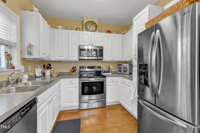 kitchen featuring appliances with stainless steel finishes, light wood-type flooring, a sink, and white cabinetry