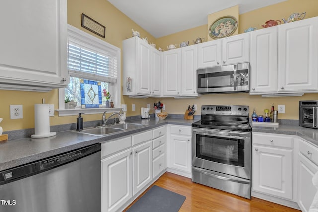 kitchen with light wood-style flooring, a sink, white cabinetry, appliances with stainless steel finishes, and dark countertops