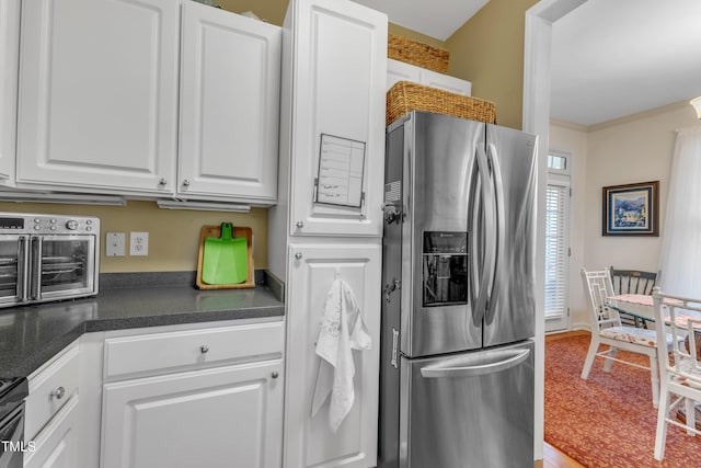 kitchen with a toaster, crown molding, dark countertops, white cabinets, and stainless steel fridge