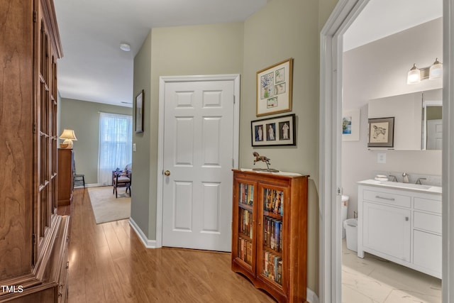 hall featuring light wood finished floors, baseboards, and a sink