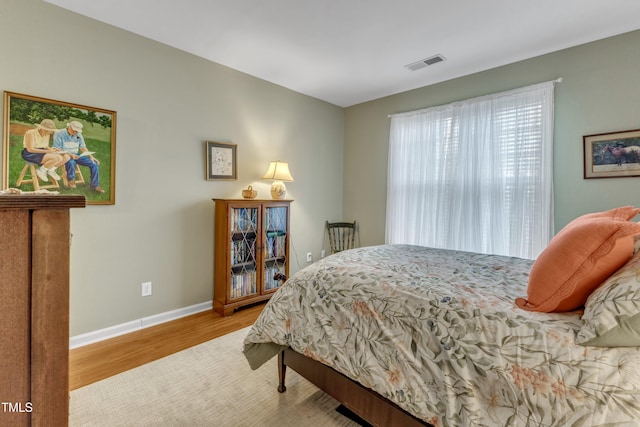 bedroom with baseboards, visible vents, and wood finished floors