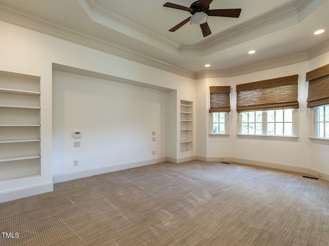 spare room with built in features, light colored carpet, ornamental molding, ceiling fan, and a tray ceiling