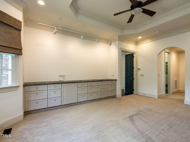 empty room featuring arched walkways, crown molding, a ceiling fan, baseboards, and light colored carpet