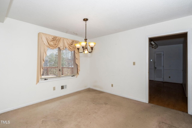 carpeted empty room featuring a chandelier, visible vents, and baseboards