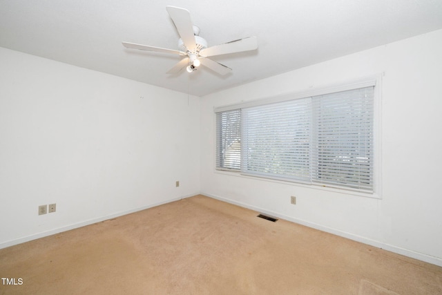 spare room with light carpet, ceiling fan, visible vents, and baseboards