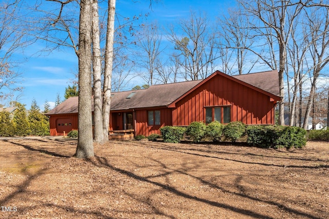 view of front facade featuring board and batten siding, roof with shingles, dirt driveway, and an attached garage