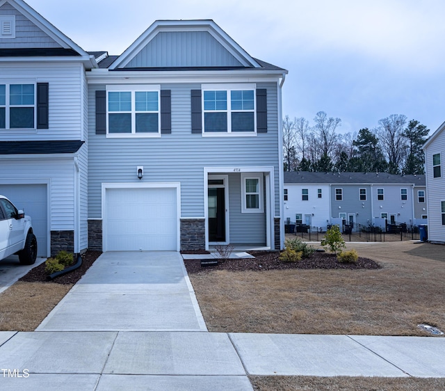 townhome / multi-family property with stone siding, an attached garage, board and batten siding, and driveway