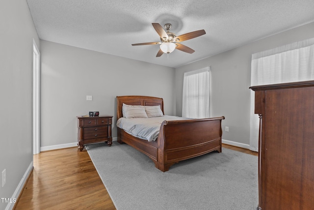 bedroom with a ceiling fan, wood finished floors, baseboards, and a textured ceiling