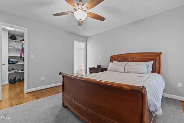 bedroom featuring a walk in closet, a ceiling fan, wood finished floors, a closet, and baseboards