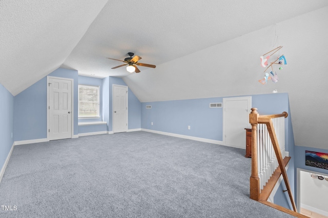 additional living space featuring a ceiling fan, visible vents, lofted ceiling, a textured ceiling, and carpet flooring