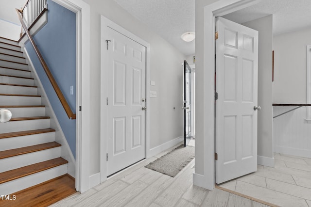 entrance foyer with stairs, baseboards, light wood-type flooring, and a textured ceiling