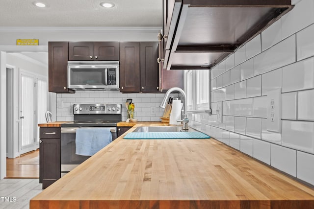 kitchen with wooden counters, ornamental molding, stainless steel appliances, dark brown cabinets, and tasteful backsplash