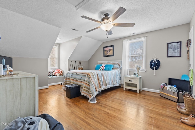 bedroom with a ceiling fan, visible vents, hardwood / wood-style flooring, vaulted ceiling, and a textured ceiling