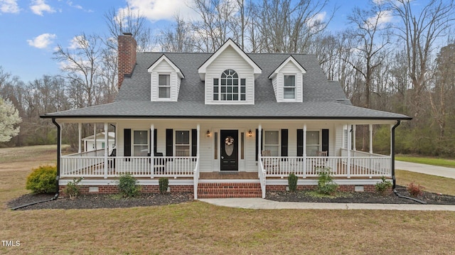 farmhouse-style home with a chimney, covered porch, a shingled roof, and a front yard