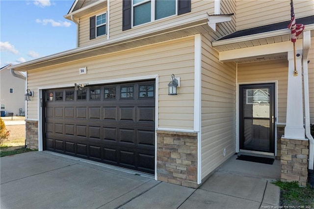 view of exterior entry with a garage, stone siding, and driveway