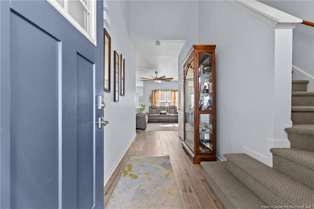 entrance foyer with light wood-style floors, baseboards, stairway, and a ceiling fan