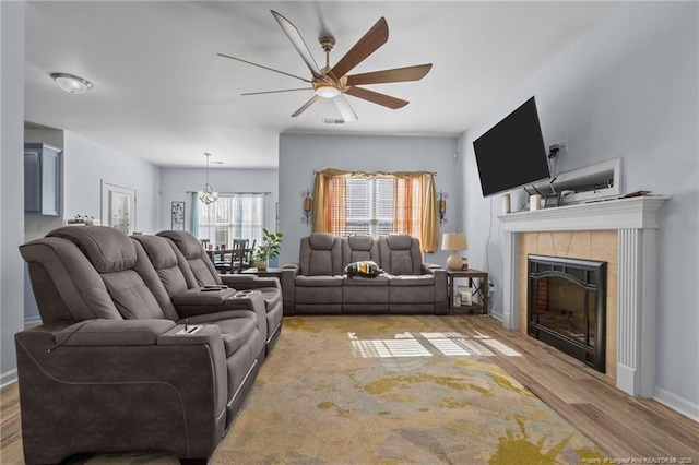 living room with a fireplace, visible vents, wood finished floors, baseboards, and ceiling fan with notable chandelier