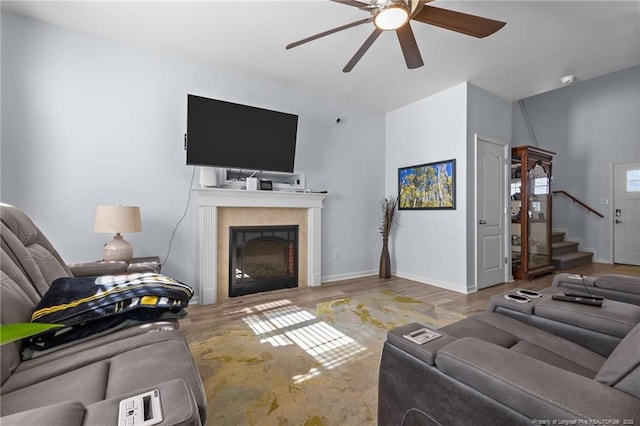 living room with baseboards, a ceiling fan, a tile fireplace, stairway, and wood finished floors