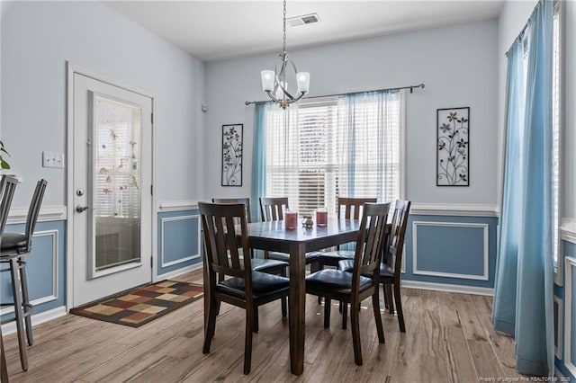 dining room with a chandelier, a decorative wall, wainscoting, and light wood-style floors