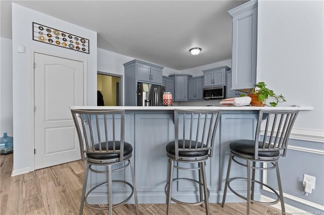 kitchen featuring light wood-style flooring, appliances with stainless steel finishes, a breakfast bar, a peninsula, and light countertops