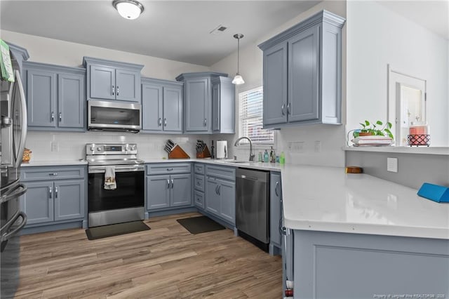 kitchen with appliances with stainless steel finishes, light wood-type flooring, a sink, and tasteful backsplash