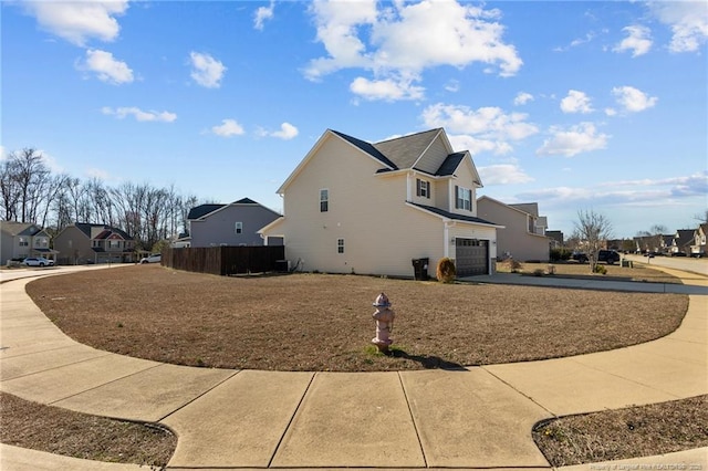 view of home's exterior featuring driveway, an attached garage, fence, and a residential view