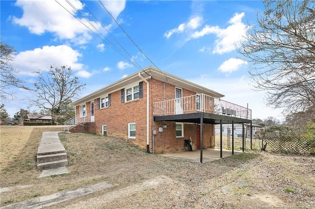 view of property exterior featuring brick siding, a patio area, a wooden deck, and fence