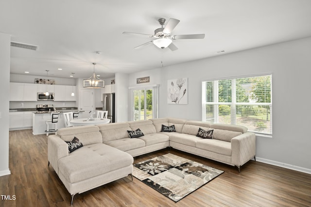 living area featuring ceiling fan with notable chandelier, visible vents, baseboards, and wood finished floors