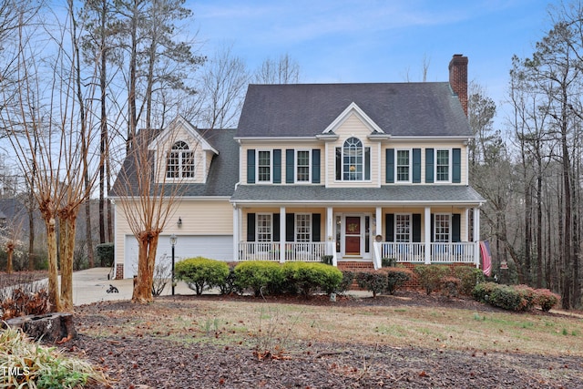 colonial home featuring roof with shingles, covered porch, concrete driveway, an attached garage, and a chimney