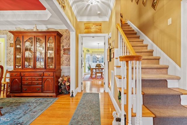 foyer entrance featuring stairway, ornamental molding, wainscoting, and wallpapered walls