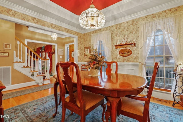 dining room with visible vents, a wainscoted wall, a notable chandelier, a tray ceiling, and wood finished floors