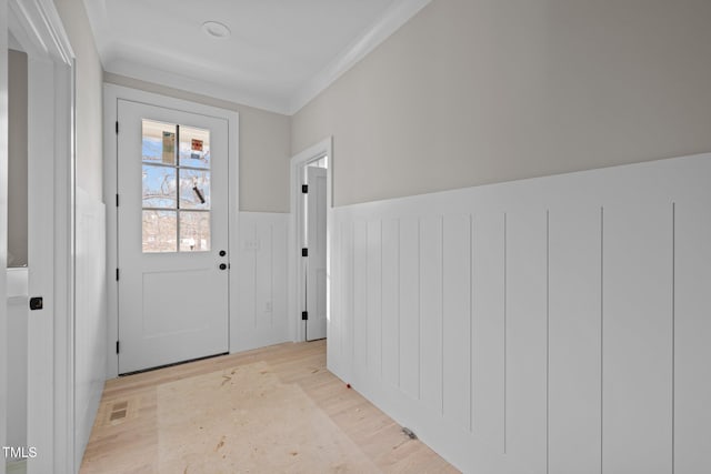 doorway to outside with visible vents, light wood-style floors, a wainscoted wall, and ornamental molding