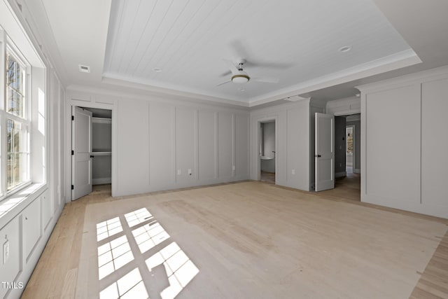 unfurnished bedroom with visible vents, a raised ceiling, light wood-style flooring, and a decorative wall