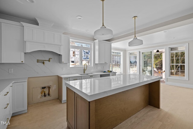 kitchen featuring light wood-type flooring, a sink, backsplash, a center island, and white cabinetry