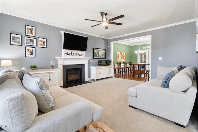 carpeted living room with a fireplace with flush hearth, crown molding, and ceiling fan with notable chandelier