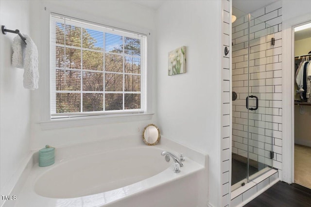 bathroom with a shower stall, a spacious closet, a bath, and wood finished floors