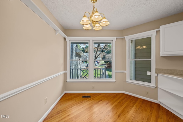 unfurnished dining area featuring light wood-style flooring, a notable chandelier, baseboards, and a textured ceiling